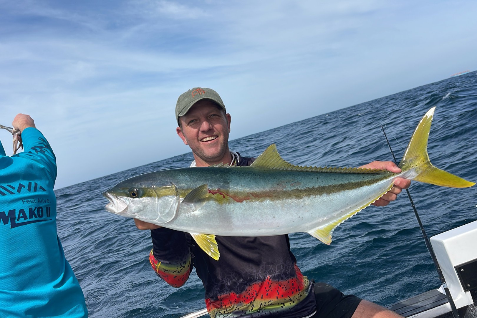 Angler holding a yellowtail on deck while crew hold bait over deep blue water