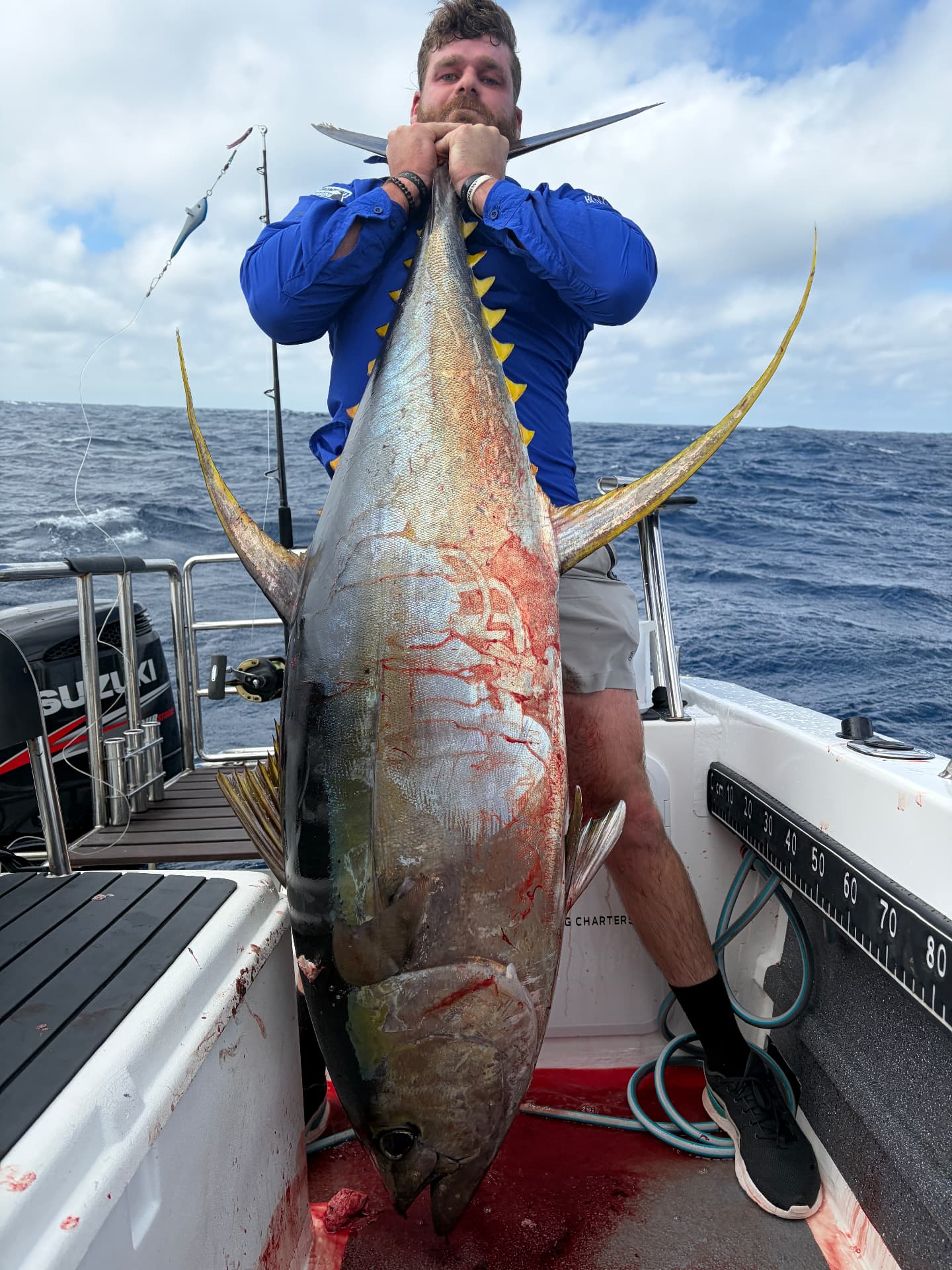 Skipper holding a large yellowfin tuna vertically on the deck of the On Point boat