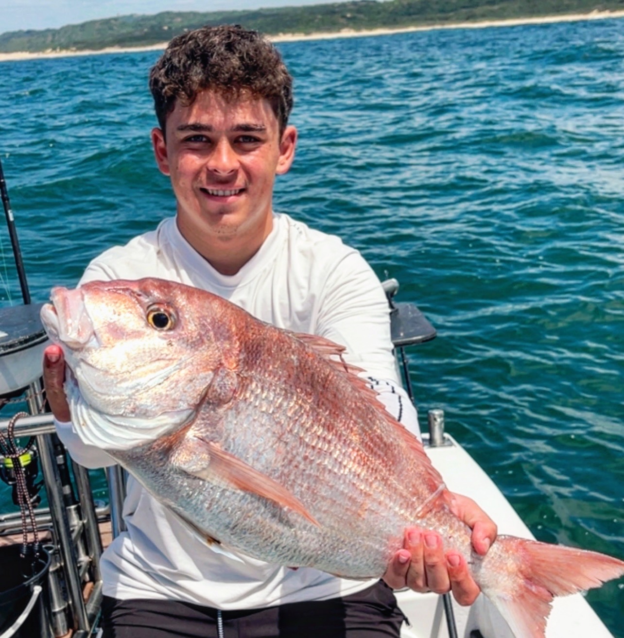 Smiling angler holding a fish on the deck with the shoreline dunes behind