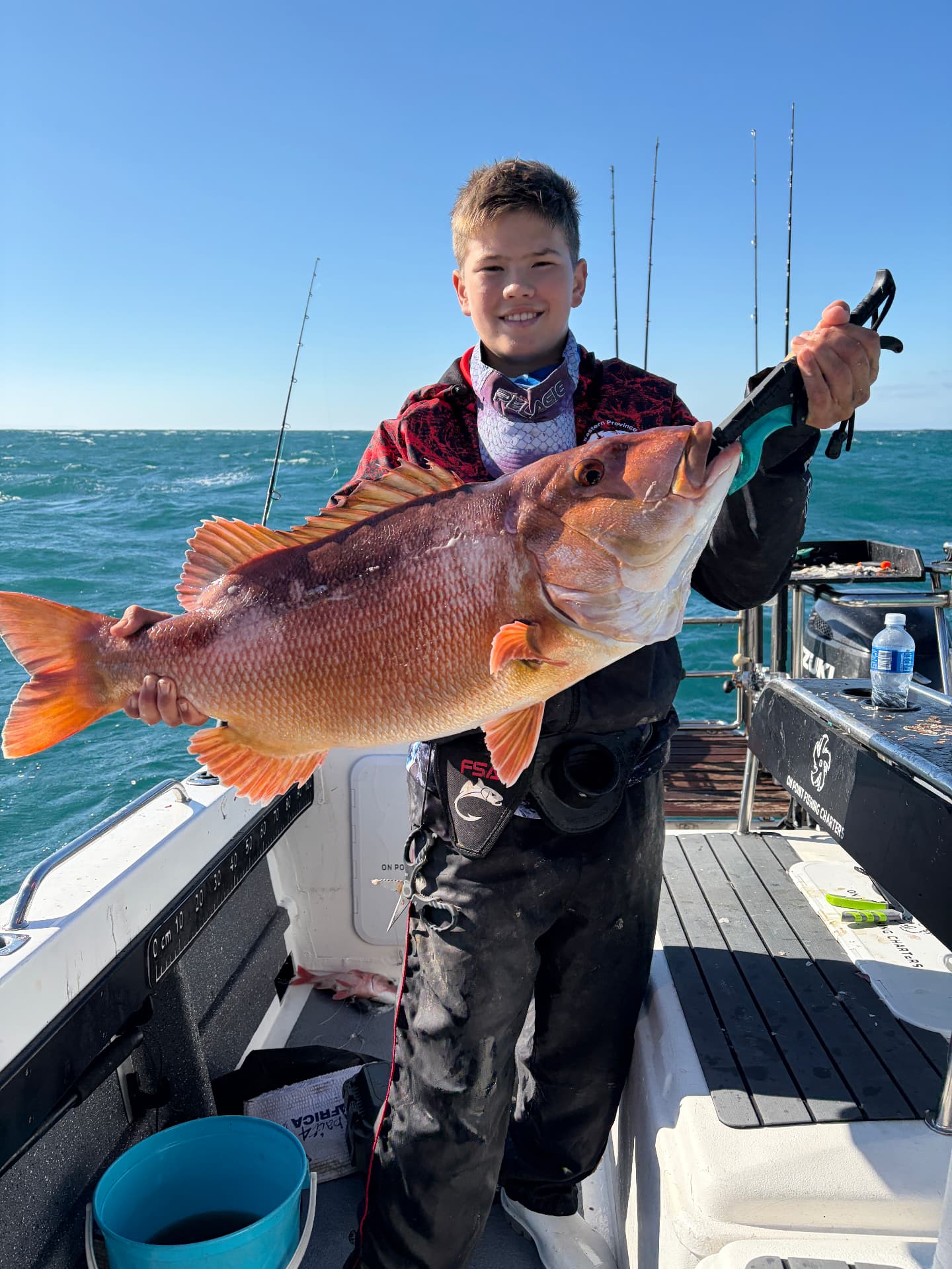 Boy holding a fish with a lip grip on the deck of the On Point boat