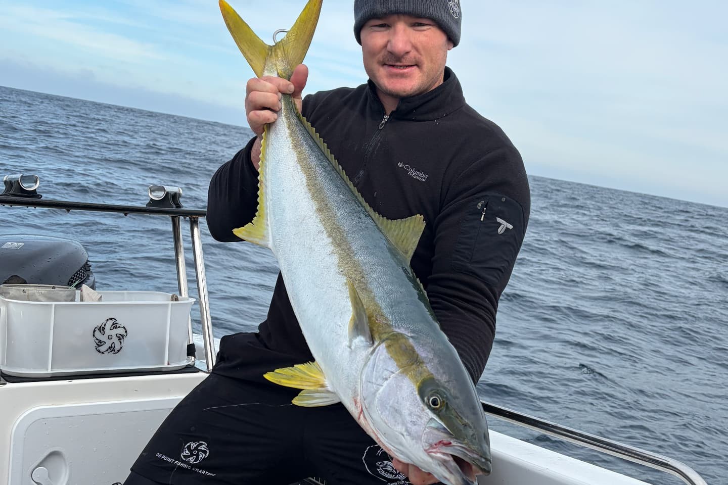 Angler holding a yellowtail on the stern of the On Point boat after a run to Bird Island